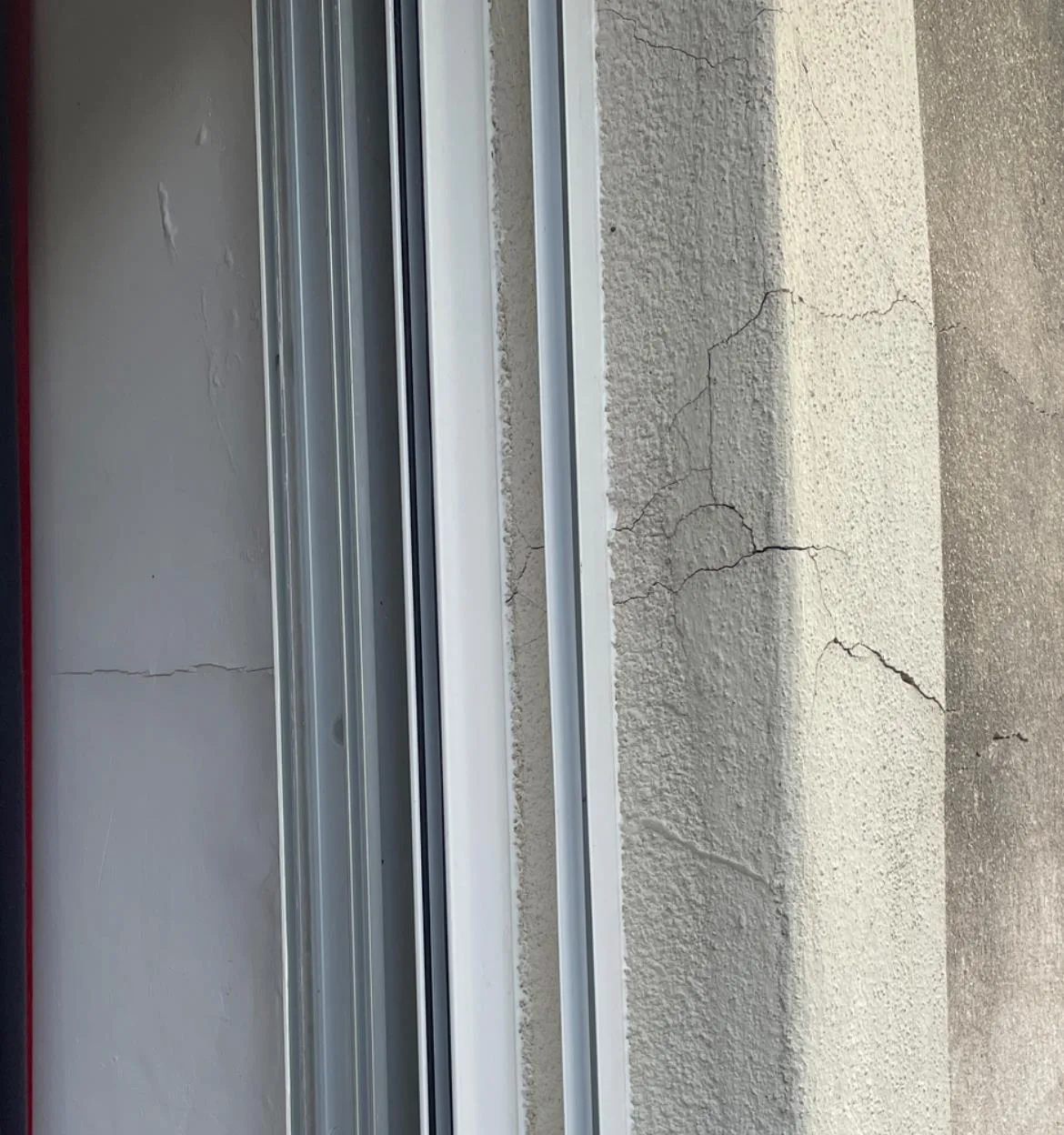 Fissures dans l'enduit à l'angle d'une baie vitrée, à l'intérieur et à l'extérieur