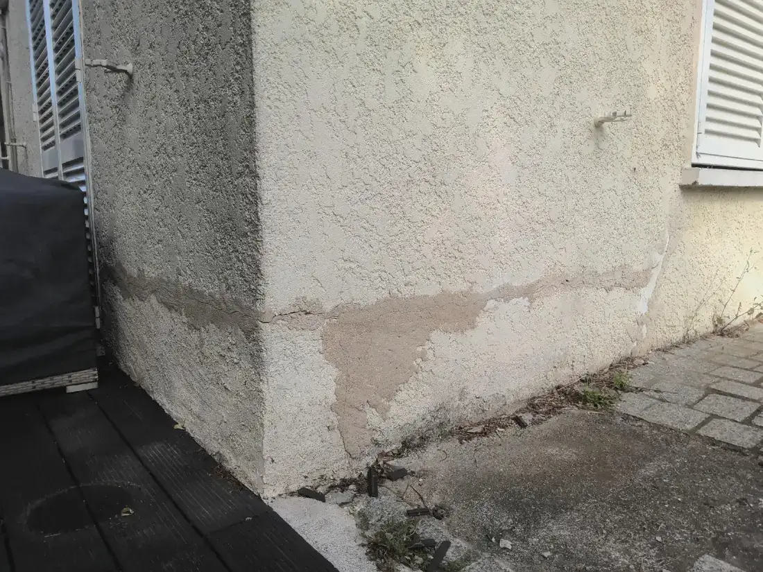 Bas de mur extérieur dégradé par l'humidité, enduit décollé en pied de façade