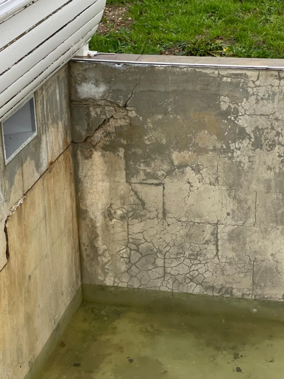 Cour anglaise inondée après la pluie, eau stagnante au pied d'un mur enterré fissuré