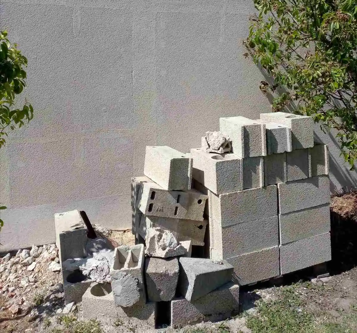 Parpaings stockés au pied d'un mur enduit, chantier de remise en état en attente de démarrage