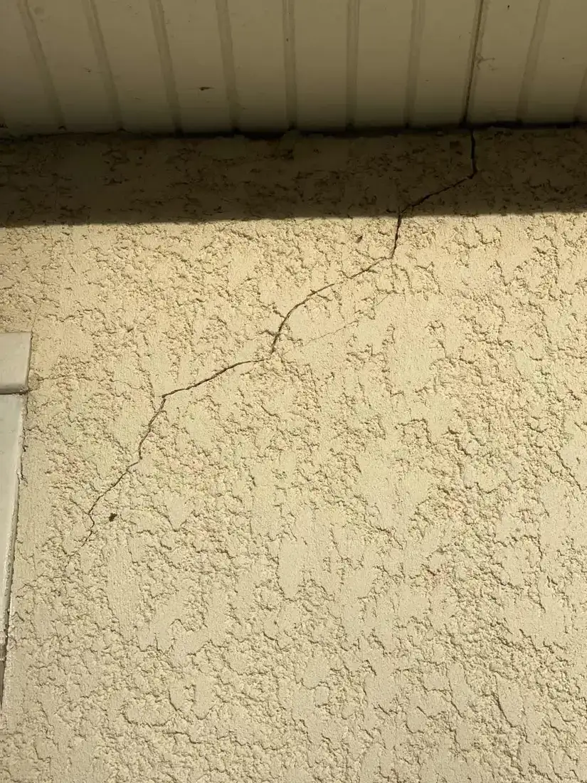 Fissure diagonale sur un enduit de façade, sous un débord de toiture