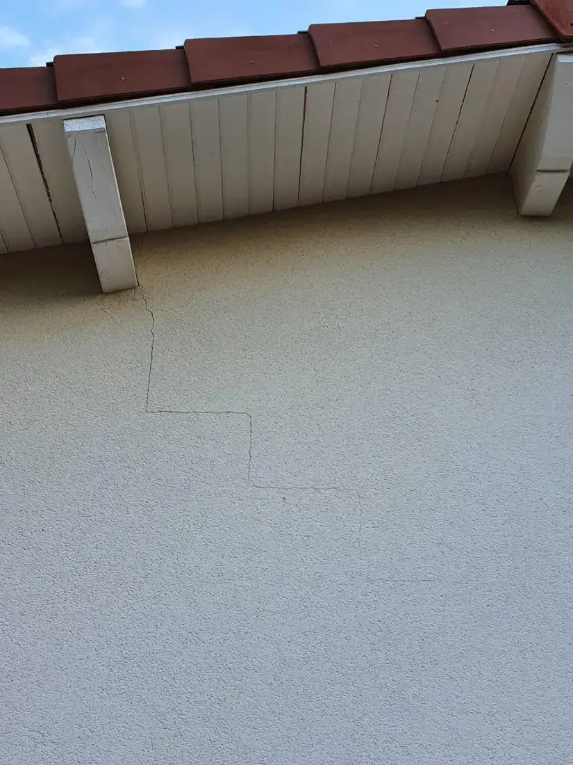 Fissure en escalier sur un enduit de façade, sous l'égout de toiture
