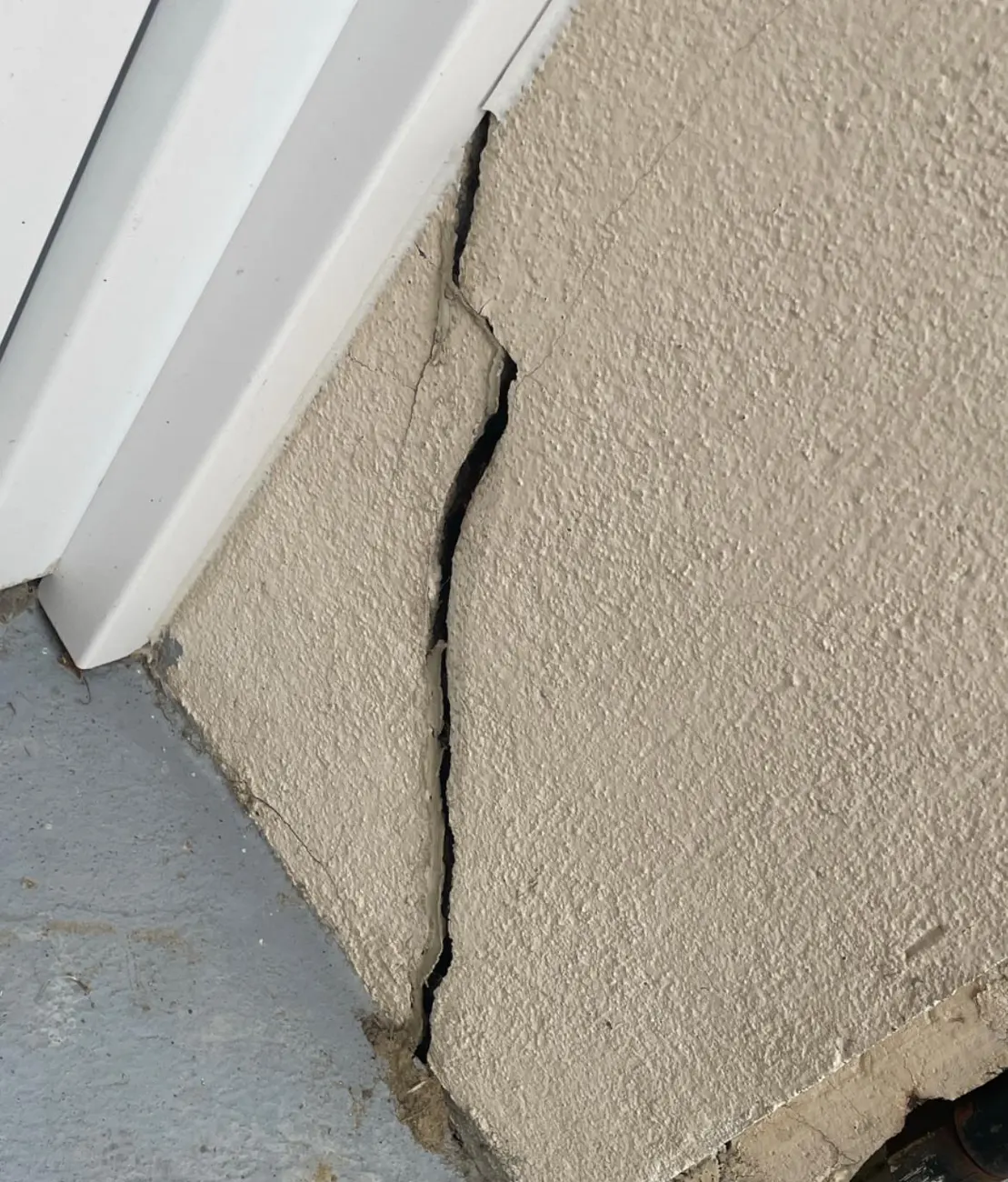 Fissure ouverte dans l'enduit au pied d'un encadrement de porte, sur une façade de maison