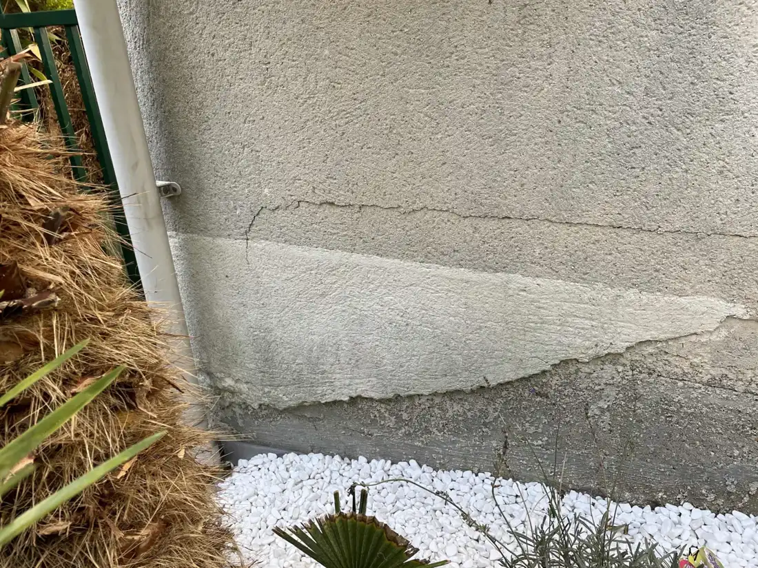 Fissure au pied d'une façade et pourtour en gravier, zone à protéger pendant une canicule