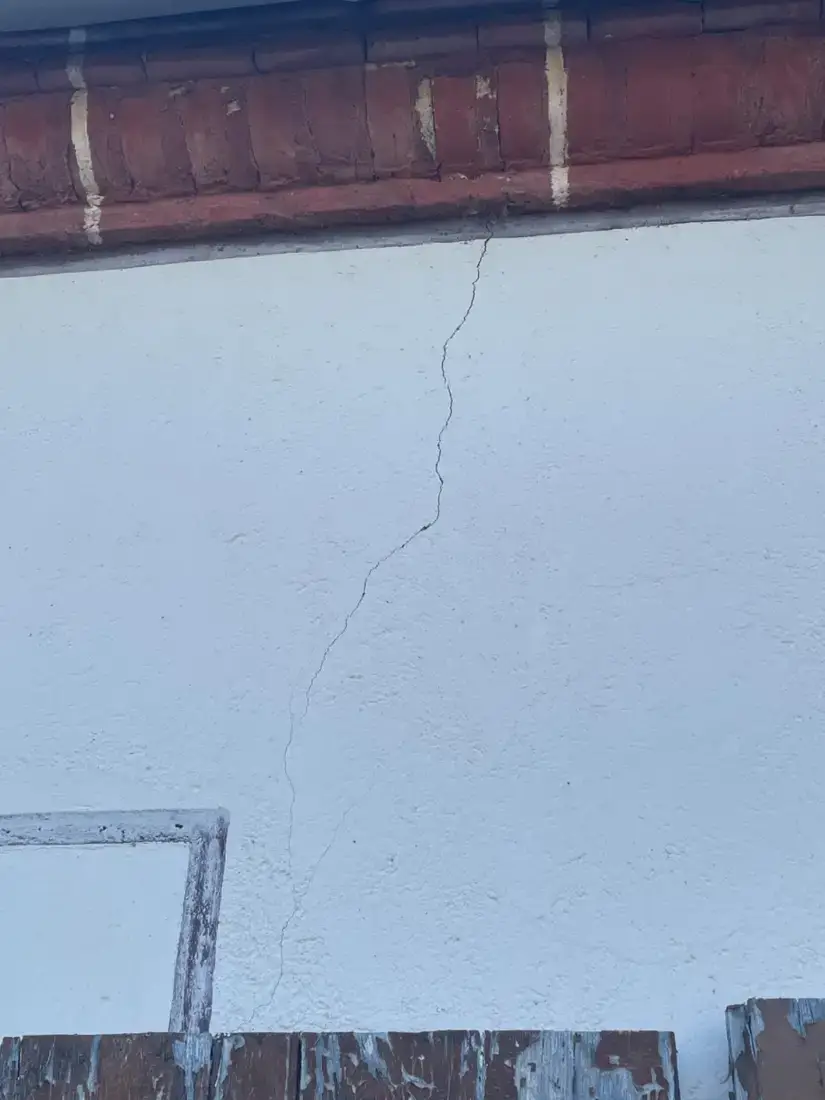 Fissure rouverte dans un enduit de façade, sous une corniche en brique