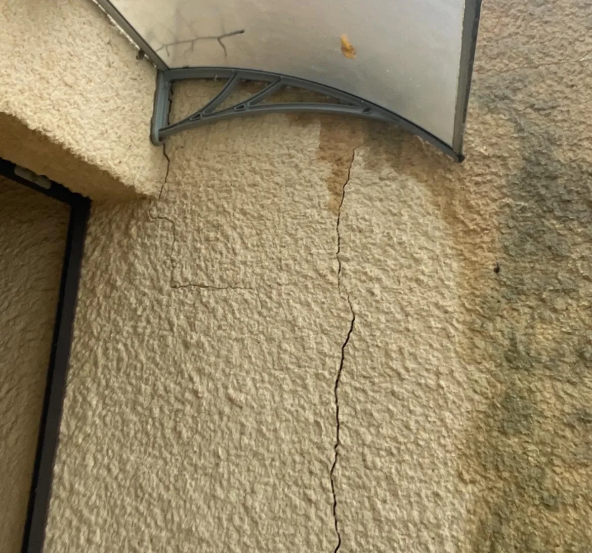 Fissure verticale dans l'enduit d'une façade avec traces d'humidité sous un auvent