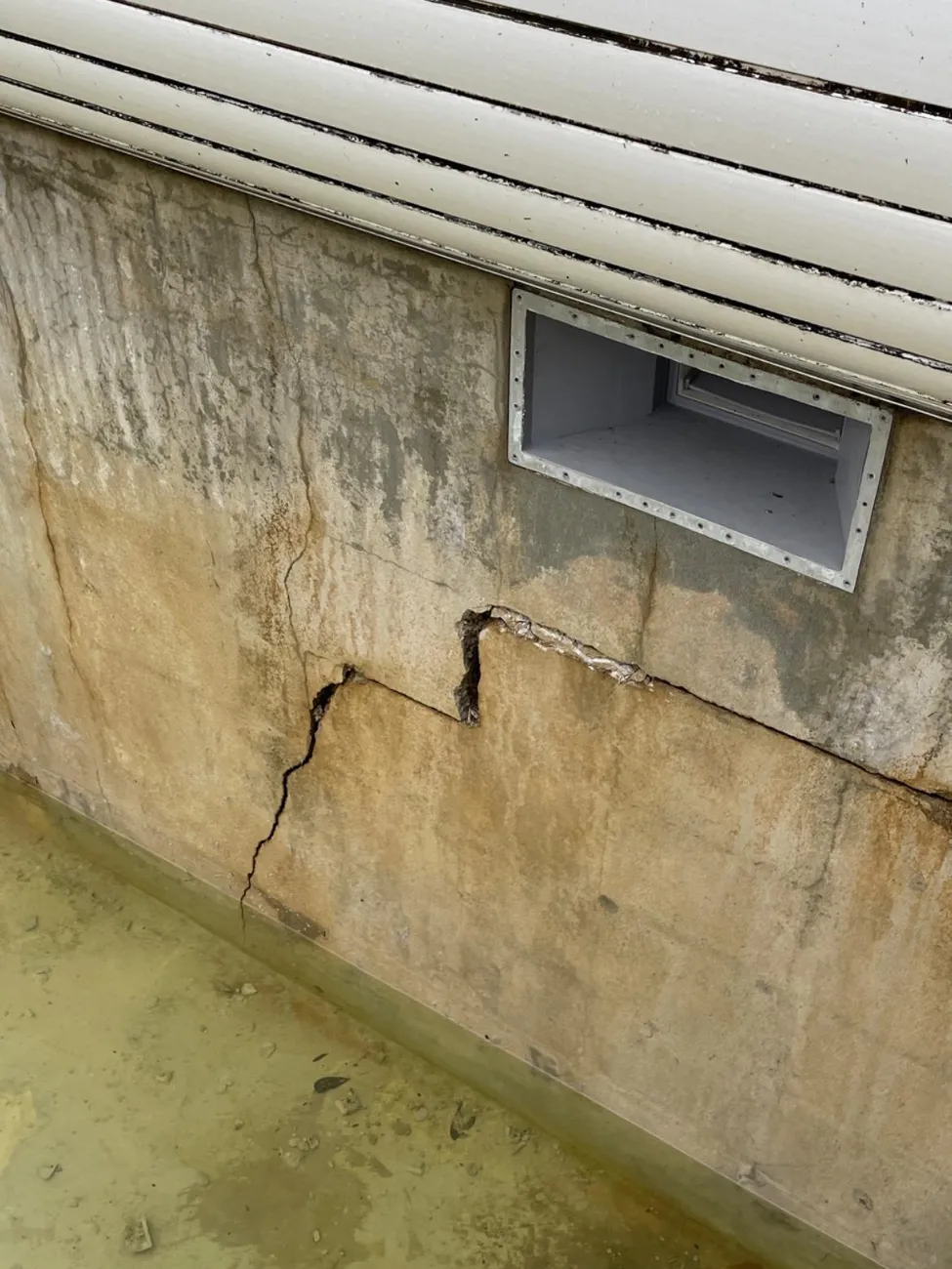 Fissure et eau stagnante au pied d'un mur enterré sous un soupirail