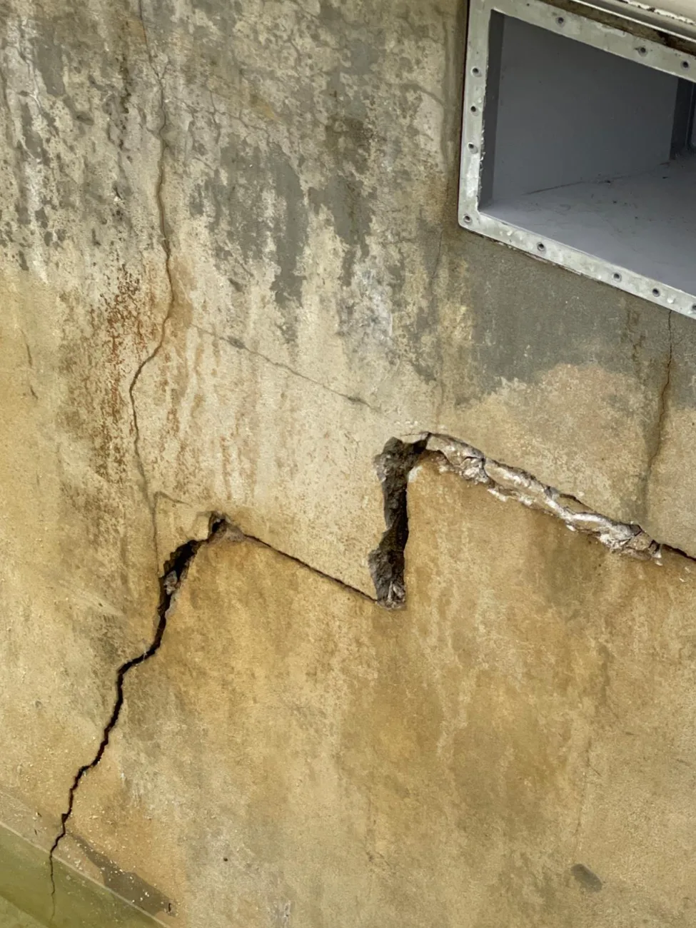 Mur enterré fissuré en escalier, traces d'humidité le long de la fissure