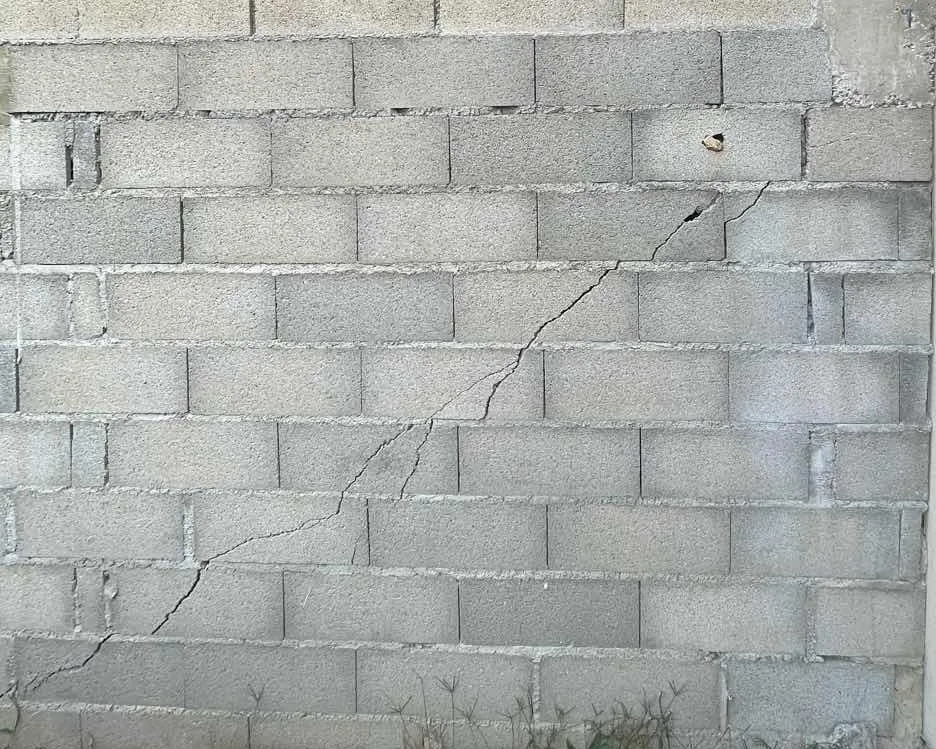 Fissure en escalier suivant les joints d'un mur en parpaing non enduit