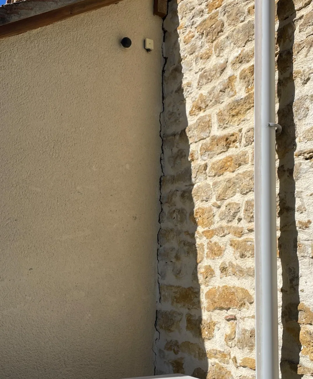 Fissure verticale à la jonction entre un mur en pierre apparente et une extension enduite