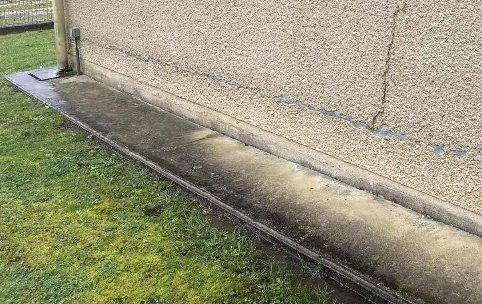 Pied de mur enterré verdi par l'eau de toiture déversée au sol le long de la façade