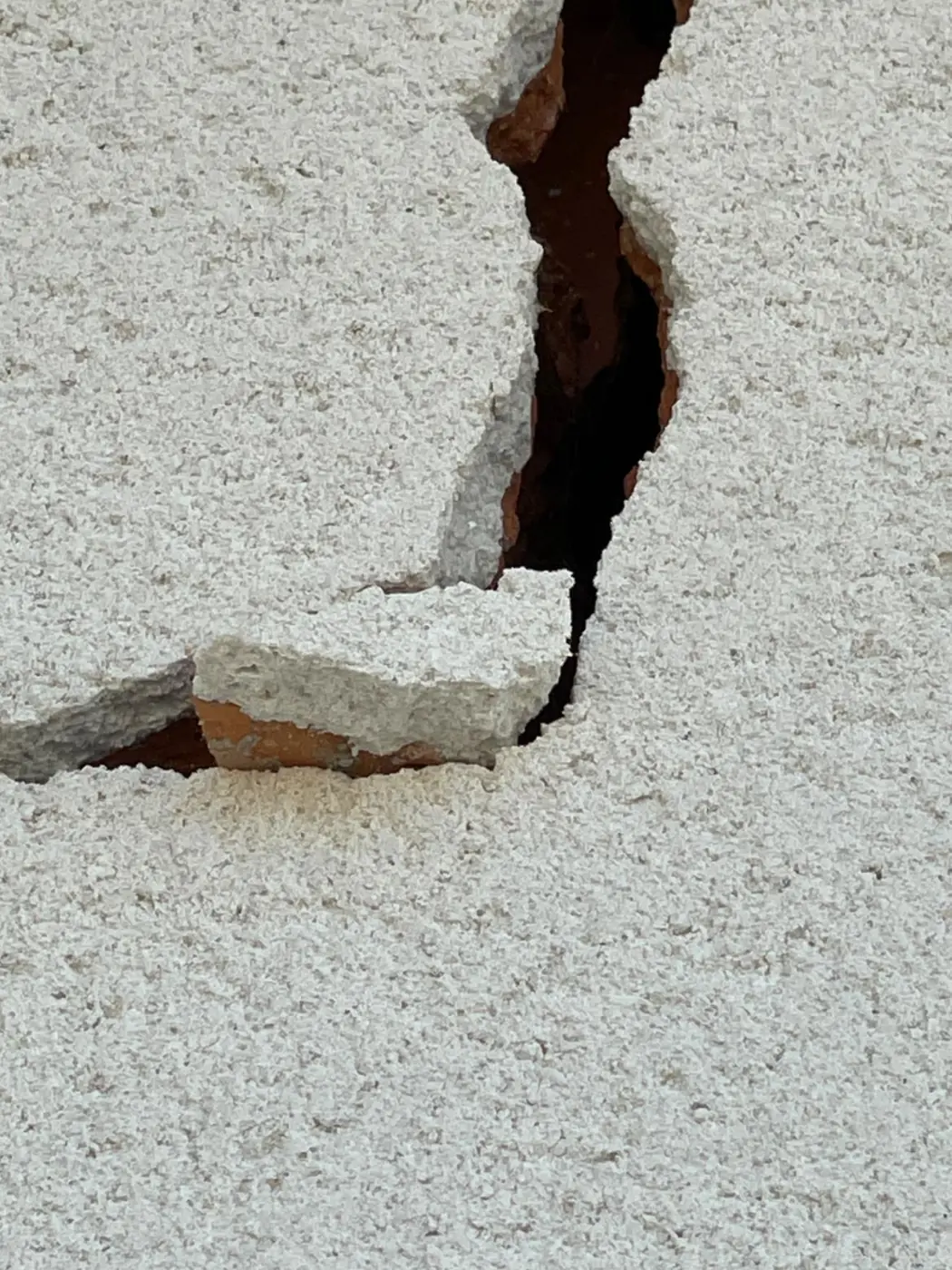 Fissure traversante exposant la brique sous l'enduit