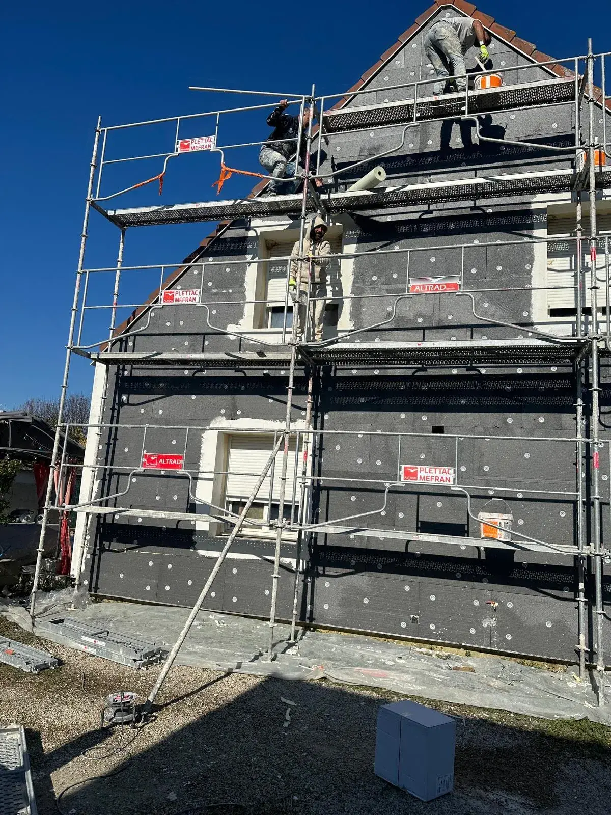Pose de panneaux isolants sur une façade lors d'un chantier d'ITE sous échafaudage